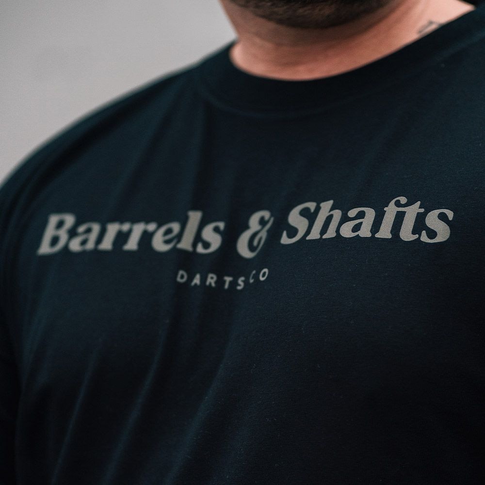 T-shirt barili e alberi - nera Das Bild zeigt ein schwarzes T-Shirt mit der Aufschrift "Barrels & Shafts". Darunter steht in kleineren Buchstaben "DARTSCO".