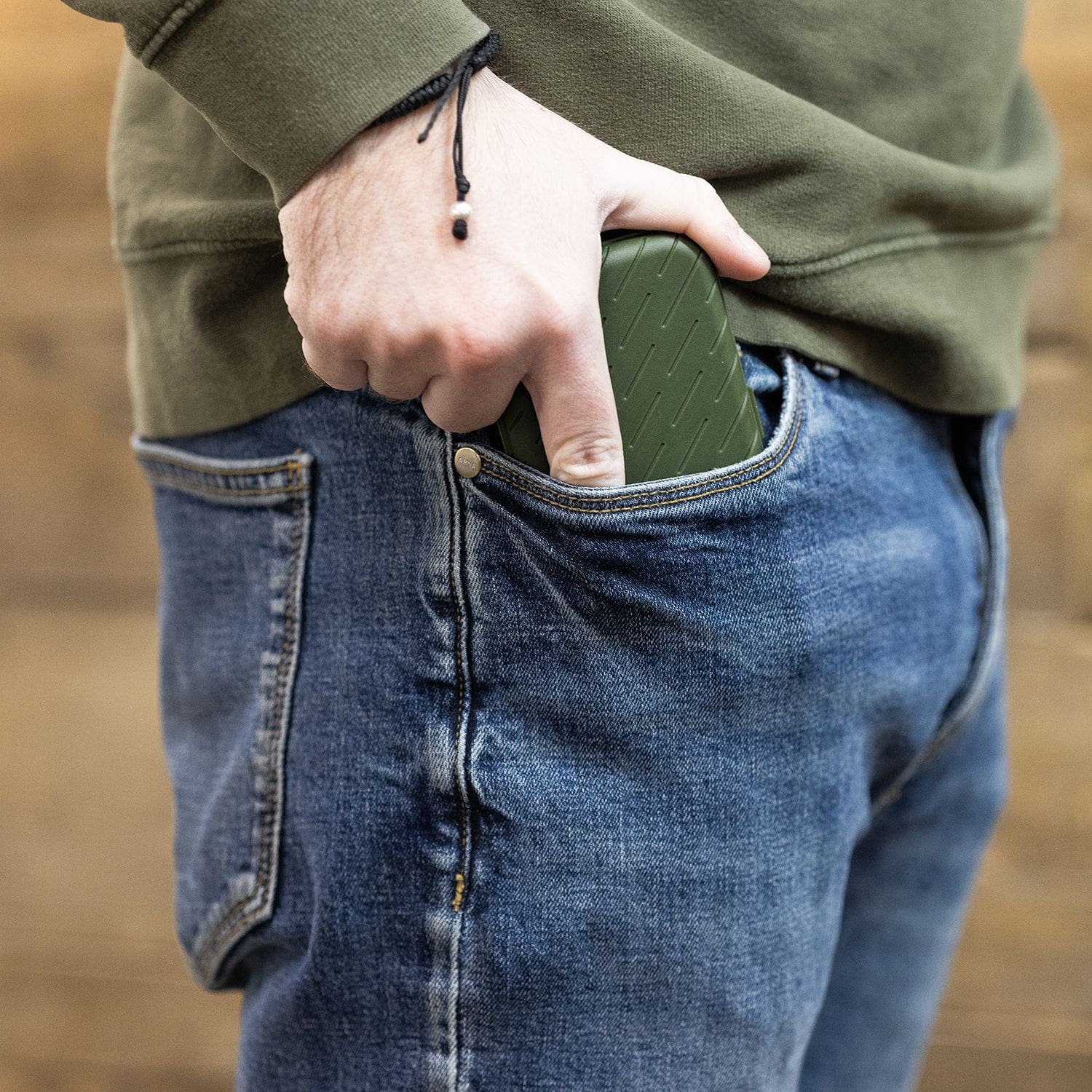 Custodia per freccette Harrows Slimcase Eine Person steckt ein grünes Etui in die vordere Hosentasche einer Jeans. Das Etui hat eine strukturierte Oberfläche und passt gut in die Tasche.