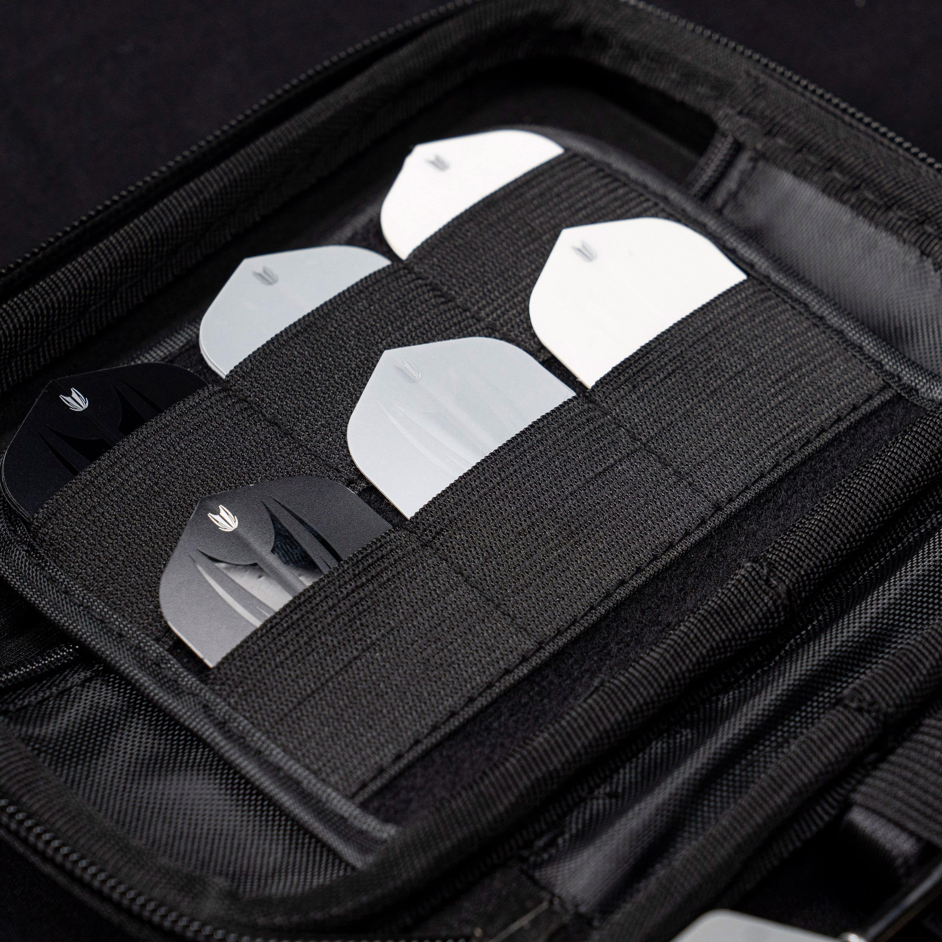 Custodia per freccette Takoma XL Ghost Series Luke Littler Das Bild zeigt das „Target Takoma Bolide XL Dartcase“, das mehrere Dart-Flights in schwarzen und weißen Farben organisiert aufbewahrt. Die Flights sind sicher in elastischen Halterungen im Inneren des schwarzen Etuis verstaut.