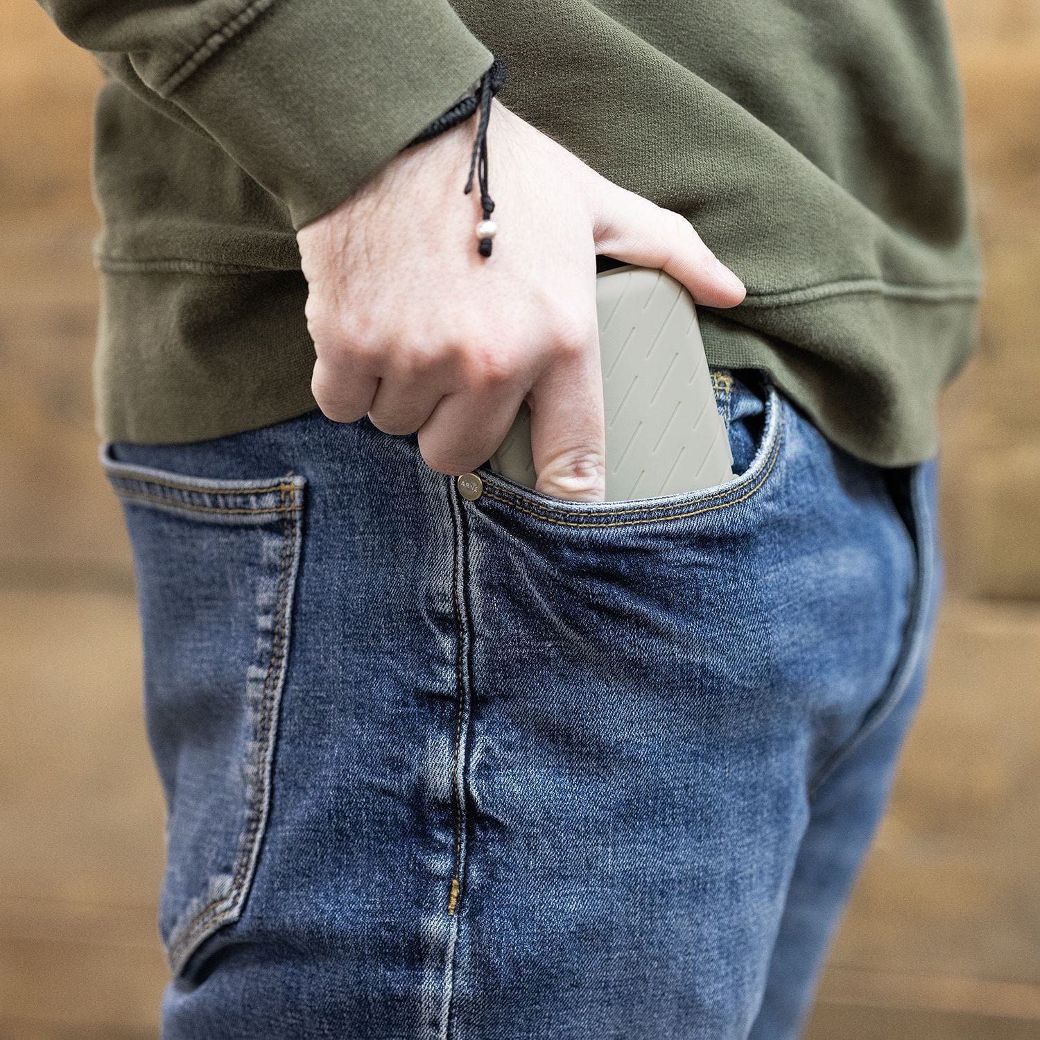 Custodia per freccette Harrows Slimcase Eine Person steckt eine graue Darttasche in ihre Hosentasche. Die Person trägt eine blaue Jeans und einen olivgrünen Pullover.