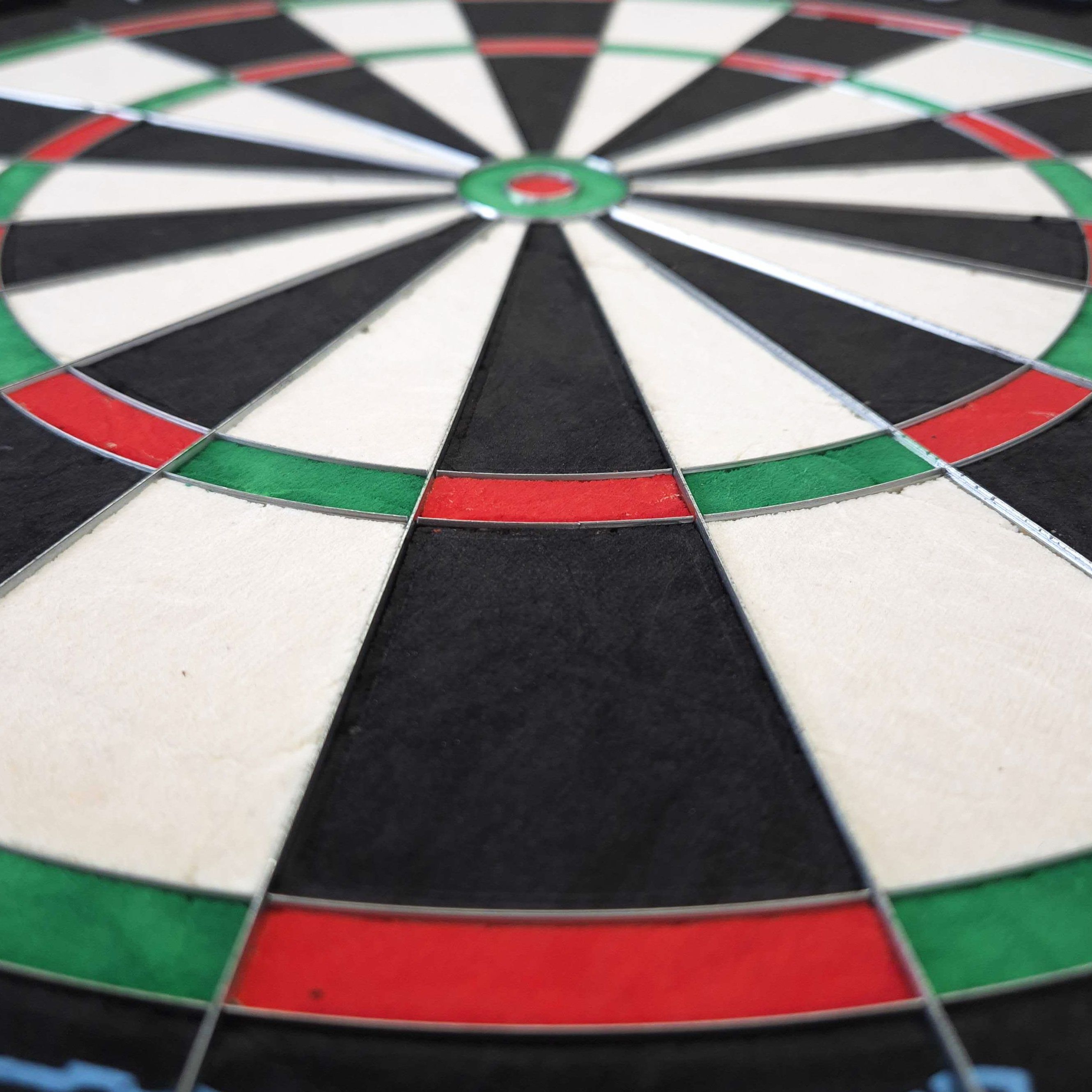 Das Bild zeigt eine Nahaufnahme eines Steeldartboards mit klar erkennbaren Farbfeldern in Rot, Grün, Schwarz und Weiß. Es handelt sich um das Produkt "Mission Samurai Infinity Steeldartboard".