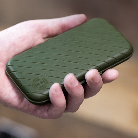 Custodia per freccette Harrows Slimcase Eine Hand hält ein schlankes, grünes Etui. Das Etui hat ein strukturiertes Muster und ein rundes Logo in der Ecke.