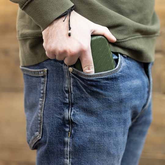 Custodia per freccette Harrows Slimcase Eine Person steckt ein grünes Etui in die vordere Hosentasche einer Jeans. Das Etui hat eine strukturierte Oberfläche und passt gut in die Tasche.